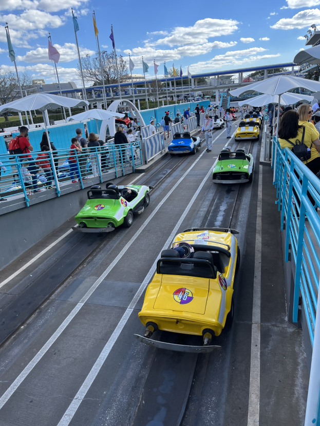 Eine Gruppe von Menschen, die in Disney's Hollywood Studios auf einer Achterbahn fahren, mit Geländern, Flaggen, Bäumen, Gebäuden und einem bewölkten Himmel im Hintergrund.