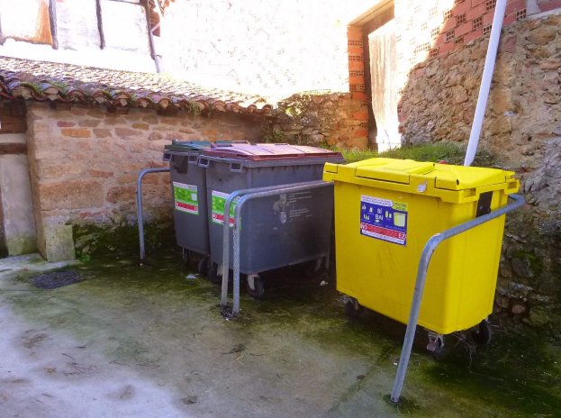 Zwei gelbe und graue Mülltonnen mit Rädern nebeneinander vor einem Gebäude mit Wand und Fenster