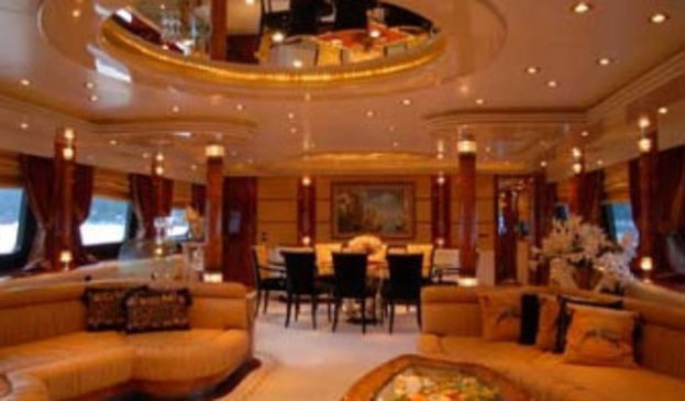 Eine Hotellobby mit Sofas, Stühlen, Tischen und Blumenarrangements im Vordergrund, Fenstern mit Vorhängen und Lampen auf beiden Seiten, einem gerahmten Bild und einer Leuchte im Hintergrund sowie einem Spiegel mit Deckenleuchten darüber.