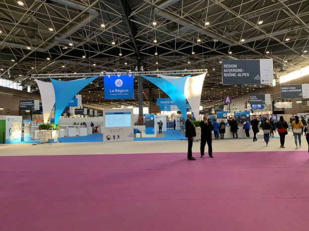 Ein großer Messestand auf der Pariser Internationalen Handelsmesse 2018 mit Menschen, die herumlaufen, von der Decke hängenden Bannern, Tischen mit Gegenständen und Deckenbeleuchtung.