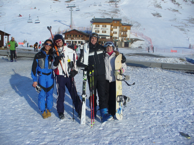 Vier Personen posieren mit Skate-Pads und Werkzeugen vor einer schneebedeckten Berglandschaft.