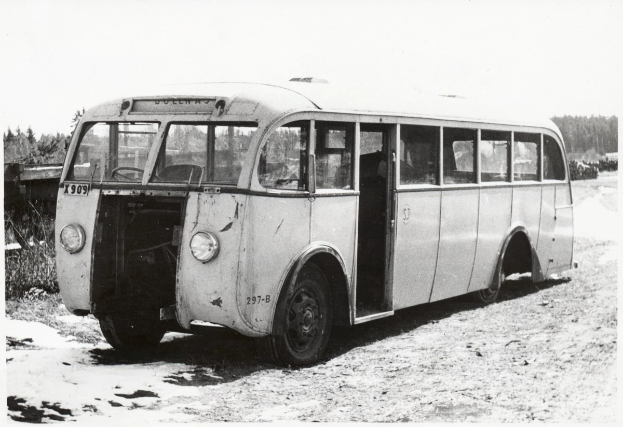 Alter Bus am Straßenrand mit Bäumen und wolkenlosem Himmel, mit einem Vorderrad.
