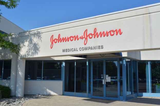 Außenansicht des Johnson & Johnson Medical Companies-Gebäudes mit Glaswänden, einem Baum auf der linken Seite, Steinen, Pflanzen und Text an der Wand vor einem klaren blauen Himmel.