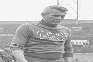 Ein Schwarz-Weiß-Foto eines Mannes, der in einem Feld steht und ein T-Shirt mit Text trägt, vor einem Stadion und einer Werbetafel, angeblich der Fußballspieler César Azpilicueta.