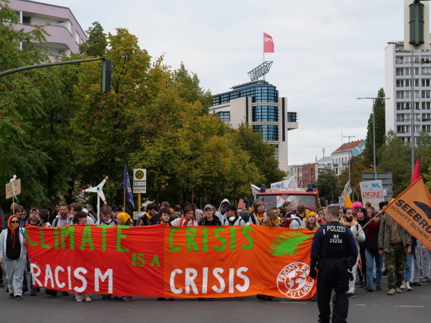 Eine Gruppe von Menschen marschiert mit einem Banner, auf dem "Klima-Krise ist eine Krise" steht, durch eine Straße.