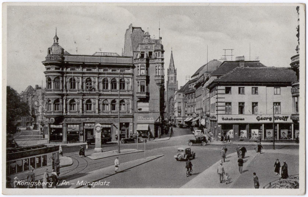 Schwarz-weiß-Foto einer belebten Münchner Stadtstraße mit Fußgängern, Fahrzeugen und Fenstern gesäumten Gebäuden, Bäumen im Hintergrund und Text unten.