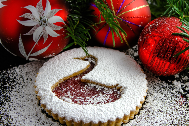Ein Close-up eines Puderzucker-bestäubten Weihnachtskeks mit einem Bissen heraus, umgeben von roten und goldenen Dekorationen und grünen Blättern.