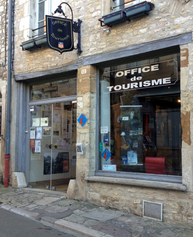 Touristenbüro mit einem 'Office de Tourisme'-Schild, Fenstern, einer Tür mit Papieren, einer Leitung an der Seite und einer Straße unten.
