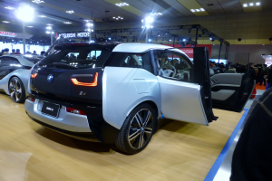 Ein weißer und schwarzer BMW i3 Elektroauto auf der Internationalen Automobil-Ausstellung in Frankfurt, umgeben von Menschen und beleuchtet von Deckenlampen, mit Informationsschildern im Hintergrund.