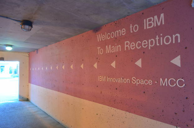 Eine Wand mit dem Text "Willkommen bei IBM" beleuchtet von Deckenlampen, im Hintergrund eine Tür mit der Aufschrift "IBM Innovation Space MCC"