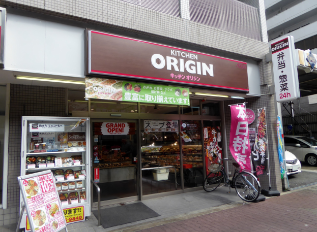 Ein Geschäft mit Glaswänden und -türen, das Lebensmittel zeigt, mit einem Fahrrad davor und Fahrzeugen auf der rechten Straße.