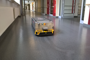 Ein Roboter, der für die Reinigung von Böden entworfen wurde, steht auf dem Boden eines Gebäudes, umgeben von Wänden, Türen, Lampen und anderen Gegenständen.