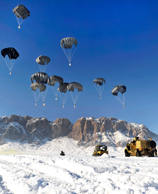 Eine Gruppe von Militärfahrzeugen, die mit Fallschirmen auf einen Hintergrund aus schneebedeckten Bergen und einem klaren blauen Himmel zusteuert.