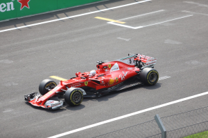 Ferraris Fernando Alonso fährt ein Formel-1-Auto beim britischen Grand Prix, umgeben von einem Zaun und Gras, mit einem sternmarkierten Sponsorboard im Hintergrund.