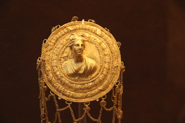Goldene Medaille mit einer Frauengestalt, mit feinen Details verziert, vor dunklem Hintergrund.