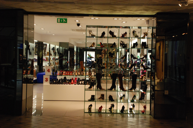 Eine Schuhgeschäftsauslage mit verschiedenen Schuhen und Sandalen auf einem weißen Tisch, einer Wand auf der linken Seite und einer Decke oben.