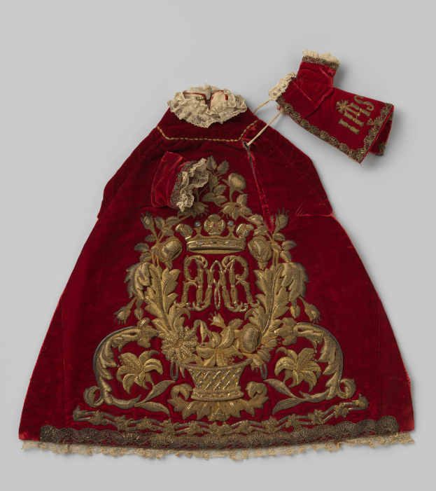 Ein roter Samtmantel mit goldener Stickerei und einer Krone, der gegen einen weißen Hintergrund gehalten wird.