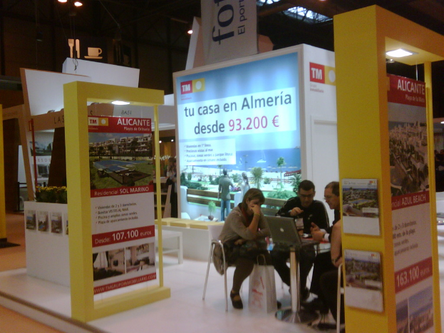 Eine Gruppe von Menschen, die um einen Tisch herum auf Stühlen sitzen und auf einen Laptop schauen, mit mehreren Flyern mit verschiedenen Anzeigen daneben.