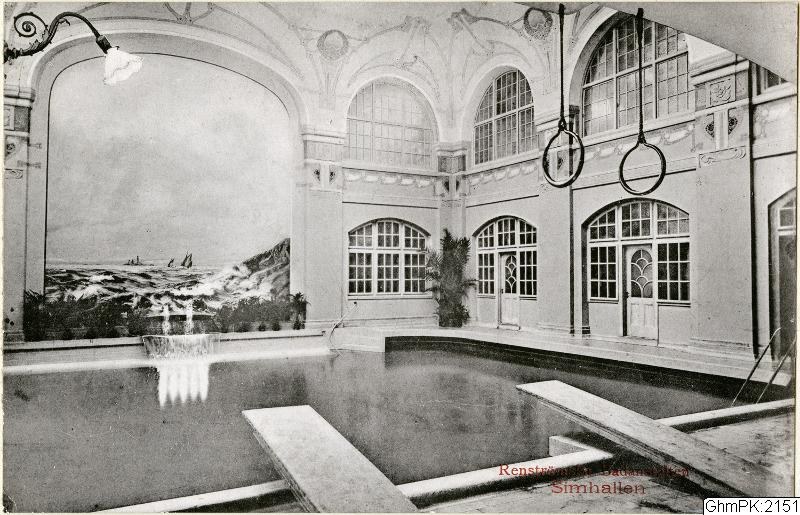 Schwarz-weiß-Foto eines großen Innenpools mit Glaswandumgebung, Hängelampe und Pflanzen, beschriftet mit "Rensburg, Deutschland - Schwimmbad."
