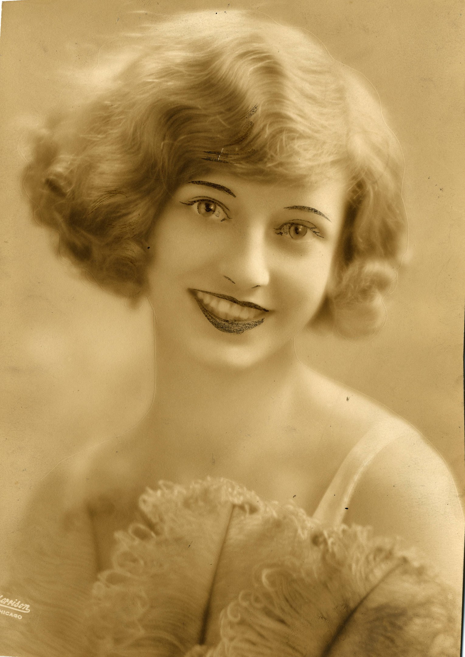 Ein Schwarz-Weiß-Foto einer Frau in einem Kleid im Stil der 1920er Jahre mit einem klassischen Bob-Haarschnitt, die warm lächelt.