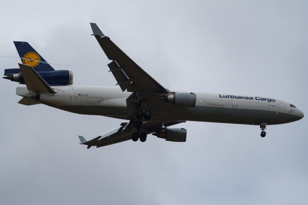 Ein Lufthansa Cargo Boeing 777-300ER-Flugzeug im Flug mit ausgebreiteten Flügeln, das durch einen Himmel mit weißen, flauschigen Wolken fliegt.