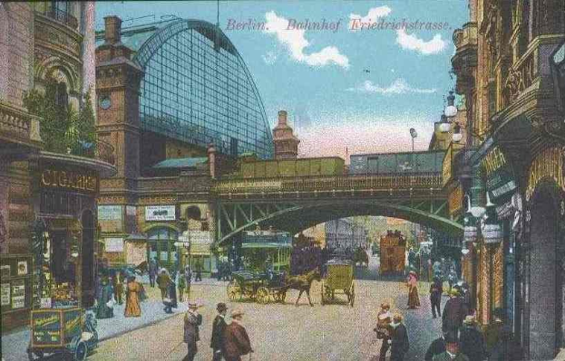 Alte Postkarte einer belebten Straße in Berlin, Deutschland, mit Passanten, Pferdewagen, Gebäuden, Laternenmasten, einer Brücke und einem bewölktem Himmel mit Text oben.