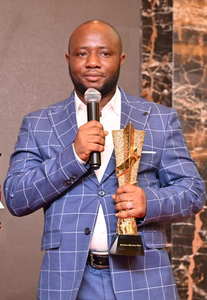 Ein Mann in einem blauen Anzug, der ein Mikrofon und eine Trophäe hält und feiert.