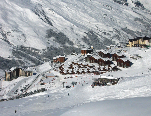 Ein malerischer Blick auf ein Skigebiet in den französischen Alpen mit schneebedeckten Bergen, Gebäuden, Bäumen und Skifahrern auf den Pisten.