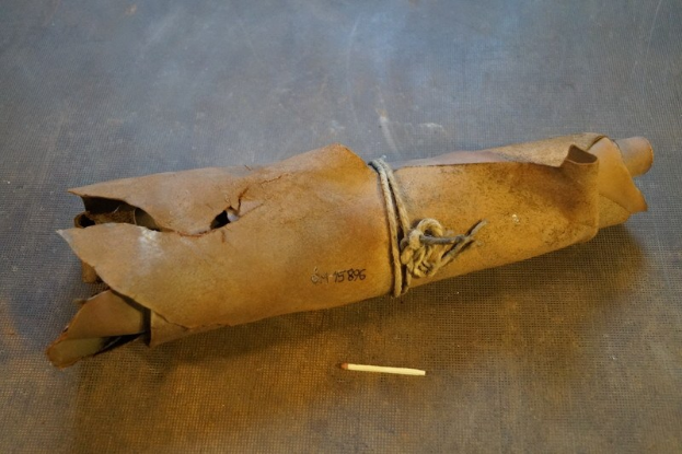 Ein brauner Papiertütenbeutel in Form einer Granate, mit einem Seil verschnürt, liegt auf einem Tisch mit einer Zigarette daneben.