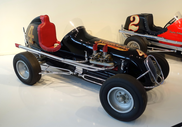 Zwei Oldtimer-Rennwagen in einem Museum ausgestellt, auf dem Boden positioniert mit einer Wand im Hintergrund.