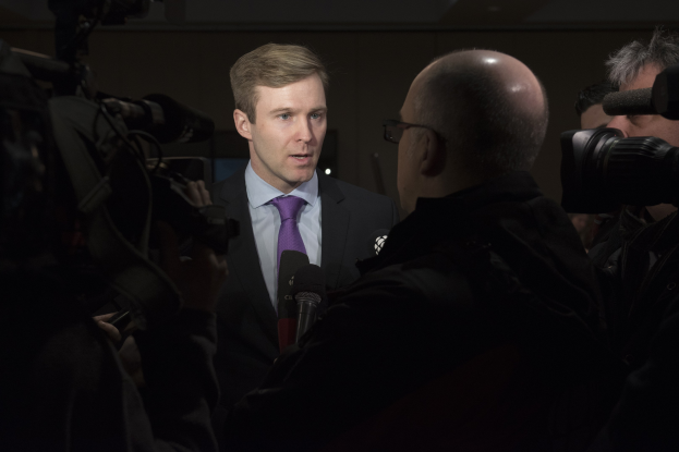Ein Mann im Anzug mit Brille spricht in ein Mikrofon, während zwei Kameraleute aufnehmen.