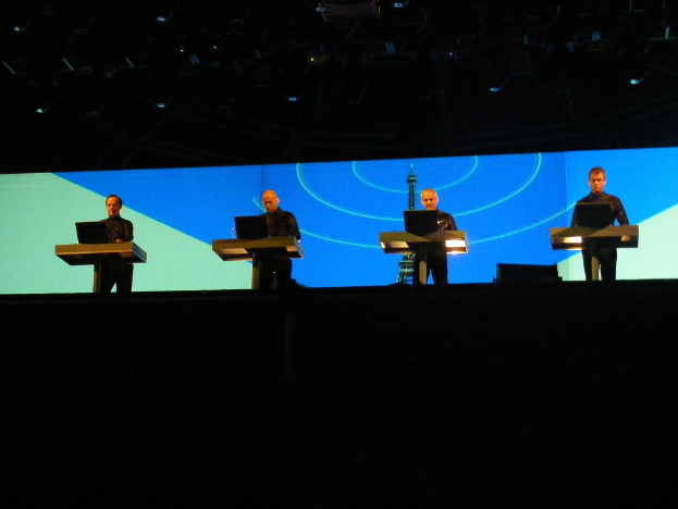 Vier Männer an getrennten Podien mit jeweils einem Laptop vor einem großen Eiffelturm-Gebäude.