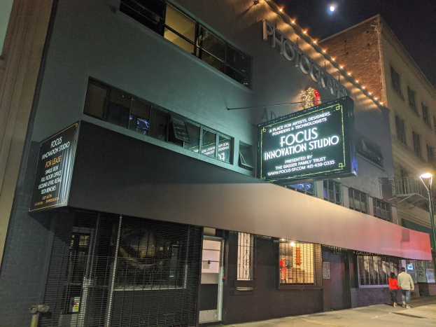 Außenansicht des Focus Innovation Studio in New York City bei Nacht mit beleuchteten Fenstern, Namensschildern und Menschen auf dem Gehweg unter Straßenbeleuchtung.