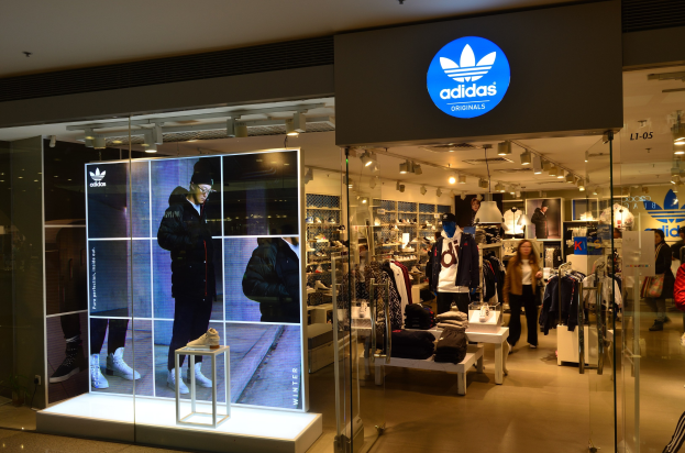 Ein hell erleuchteter Adidas Originals Store in einem Einkaufszentrum mit Schaufensterpuppen, aufgehängten Kleidern und Schuhen auf Ständern mit dem Adidas-Logo auf einer Tafel.
