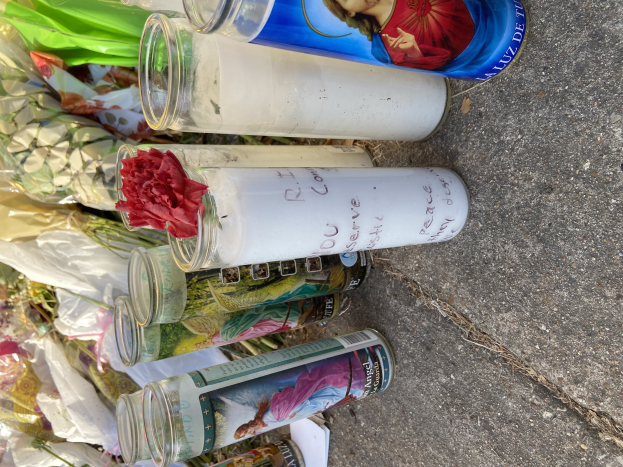 Provisorisches Denkmal mit Glasflaschen mit Bildern und Text, einem Blumenstrauß und angezündeten Kerzen am Straßenrand.