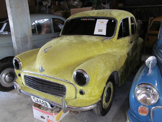 Mehrere Oldtimer stehen vor einer Wand mit verschiedenen Zubehörteilen, wobei auf der linken Seite eine Säule zu sehen ist.