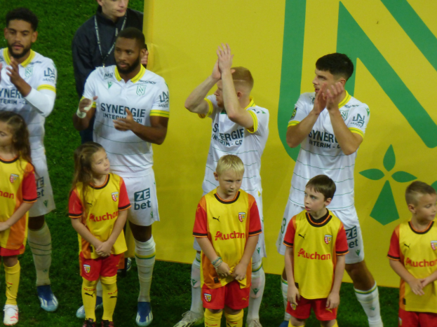 Eine Gruppe von Füßballspielern in Uniformen, die auf einem Feld klatschen, mit einem "Ligue 1"-Schild im Hintergrund, feiern einen Sieg.