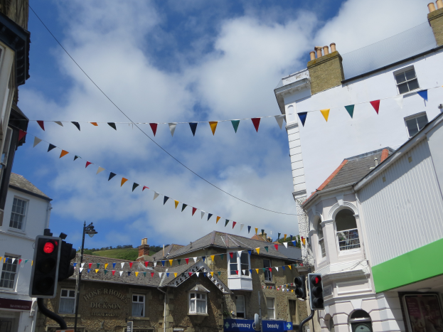 Eine Stadtstraße mit Gebäuden auf beiden Seiten, Ampeln und Texttafeln unten, einer Straßenlaterne und einem Verkehrssignal in der Mitte mit buntem Schmuck und einer bewölkten Himmel im Hintergrund.