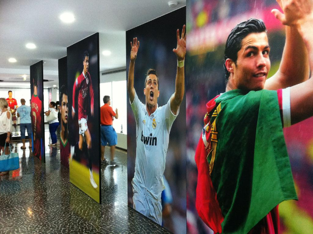 Ein Banner mit dem Fußballspieler Rolando, auf dem Menschen links neben einem Tisch und Lichter oben zu sehen sind.
