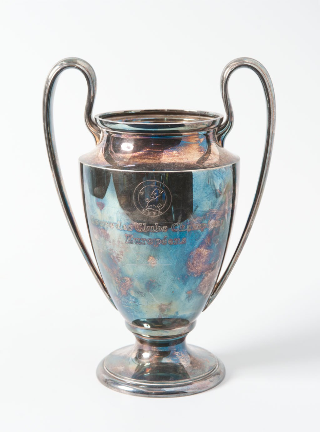 Der UEFA-Champions-League-Pokal, ein silberner und blauer Stahlbecher mit zwei Griffen, der mit "UEFA Champions League" beschriftet ist, vor einem weißen Hintergrund.