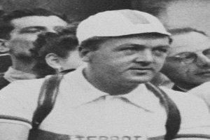 Schwarzes und weißes Foto eines Mannes in einer Mütze und Hosenträgern, der vor einer Gruppe von Menschen steht, der mutmaßlich ein legendärer Fußballspieler ist.